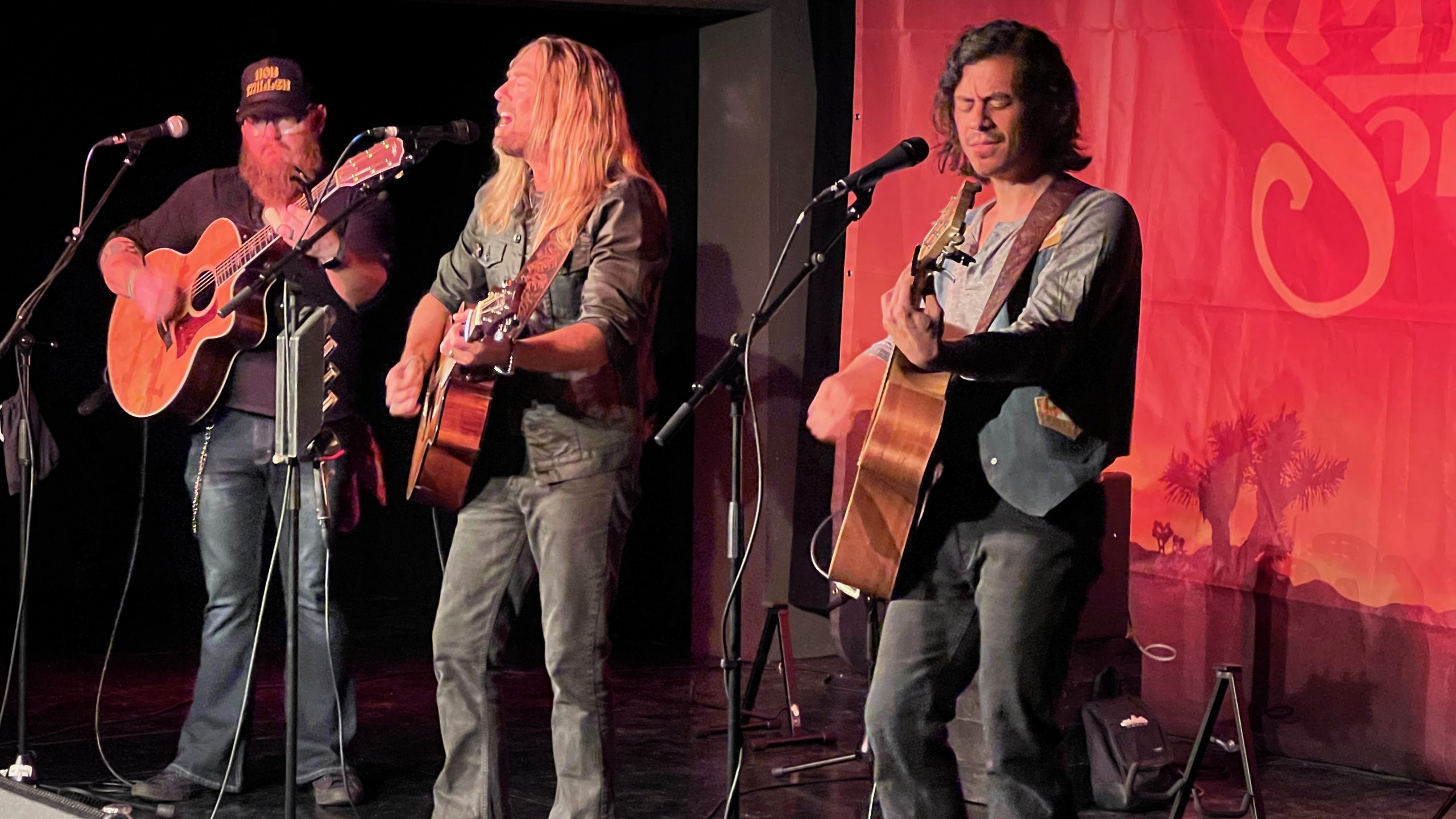 Die drei Musiker von High South stehen auf der Bühne. Das Foto ist diesmal von einer geringeren Entfernung aus aufgenommen. Die Bühne ist in rotes Licht getaucht.