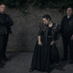 Auf dem dunkel gehaltenen Bild sieht man die drei Musiker der Band Schwarzes Edelweiss. Die Sängerin sowie die anderen beiden Musiker sind ganz in Schwarz gekleidet