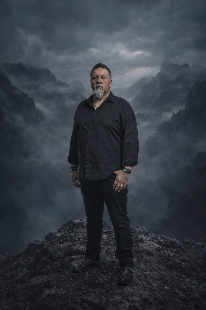 Der Gitarrist steht in lässiger Haltung vor dem dunklen Hintergrund