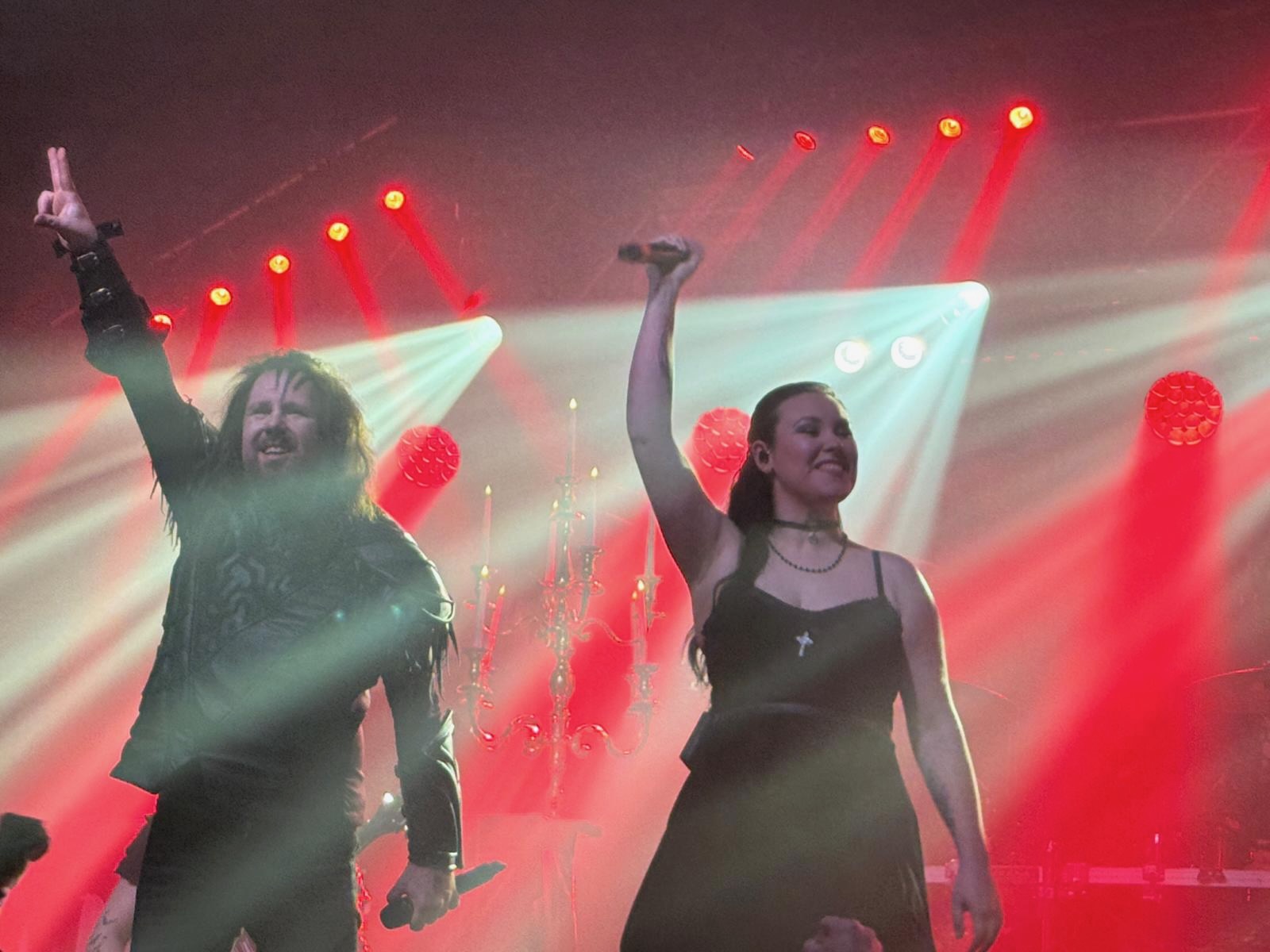 Auf der rotdurchfluteten Bühne stehen der Sänger und die Sängerin von Hammer King und heben ihre Mikros in die Höhe, um sich beim Publikum zu verabschieden.
