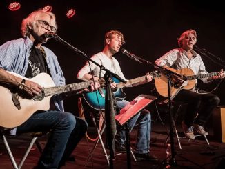 Auf dem Foto sieht man die drei Musiker Ulli Bär, Andy Baum und Matthias Kempf mit ihren Gitarren auf einer Bühne sitzen